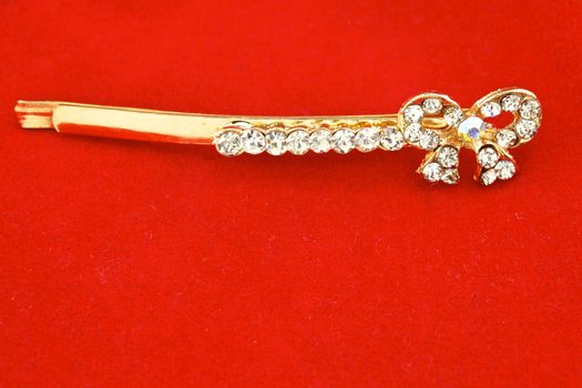 Gold hair clip and diamond as bow on red background.