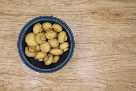 Champignon mushrooms are in blue bowl put on wood background.