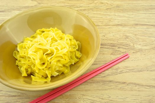 Big yellow noodle scald in brown bowl and chopsticks with wood background.