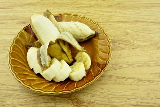 Cultivated banana peel and slice put on brown dish with wood background.