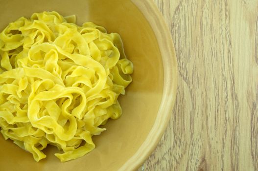 Close up big yellow noodle scald in brown bowl with wood background.