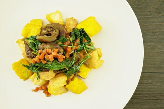 Tofo fried with carrot, basil and mushroom in plate on wood background.