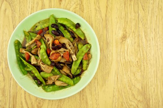 Green pea fried with red bean, tomato and mushroom on wood background.
