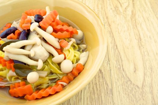 Close up soup big yellow noodle with tofu, carrot, red bean and shimeji mushroom on wood background.