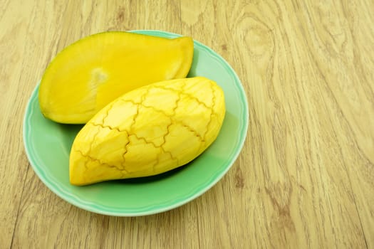 Slice half ripe mango on green dish with wood background.