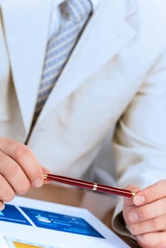 businessman holding a pen in hand, in front of him laid paper business financial charts