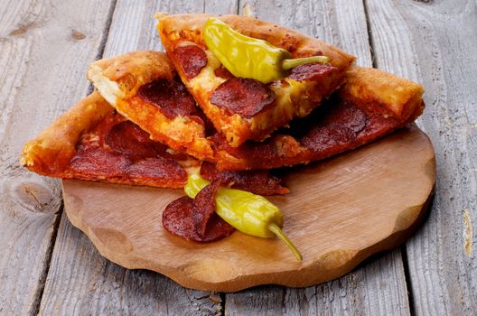 Stack of Tasty Pepperoni Pizza Slices with Two Jalapeno Peppers on Wooden Plate closeup on Rustic Wooden background