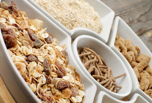 Muesli with Raisins and Nuts, Oat Flakes and Bran in White Plates closeup on Wooden background