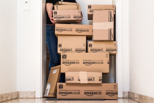 OSTFILDERN-SCHARNHAUSEN, GERMANY - MAY 18, 2014: A woman is horrified by a large stack of parcels by Amazon.com in different sizes waiting in front of the entrance door to her flat on May, 18, 2014 in Ostfildern-Scharnhausen near Stuttgart, Germany. This conceptual photo can serve different purposes: It might demonstrate the domination of Amazon.com in the area of online shopping or the trend in general to shop online for all the different items you need in your personal life.