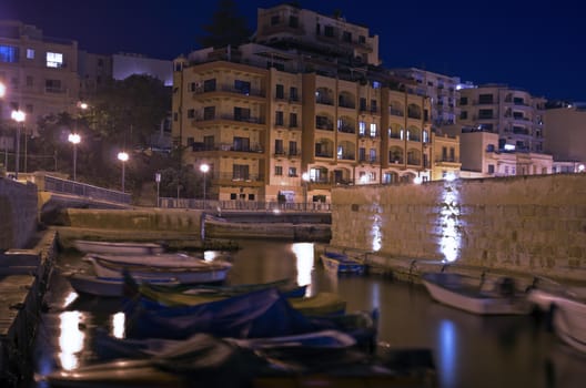 Boat shelter and modern buildings on the waterfront in the old fishing village of St Pauls Bay by night - San Pawl il-Baħar, Malta.