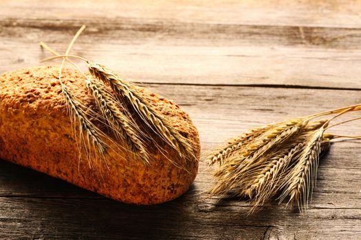 Rye spikelets and bread on wooden background