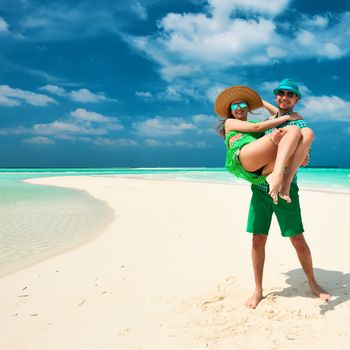 Couple in green on a tropical beach at Maldives. Man in holding woman on his arms.