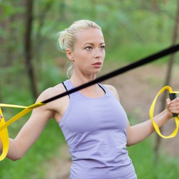 Young attractive woman does suspension training with fitness straps outdoors in the nature.