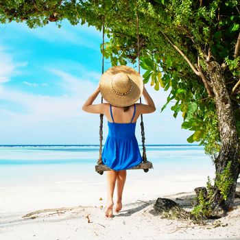 Woman in blue dress swinging at tropical beach