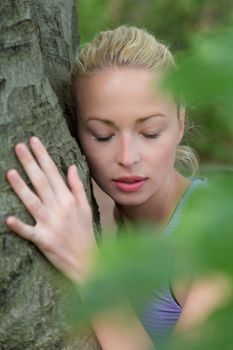 Relaxed young lady embracing a tree receiving life energy from the nature.