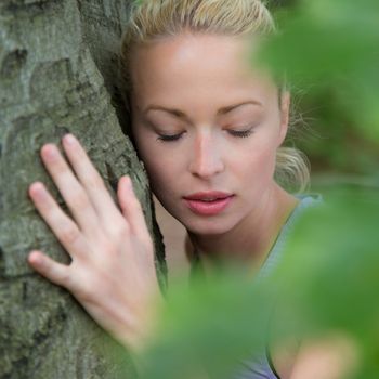 Relaxed young lady embracing a tree receiving life energy from the nature.