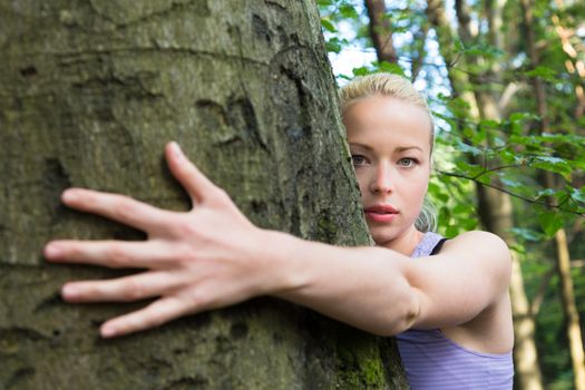 Relaxed young lady embracing a tree receiving life energy from the nature.