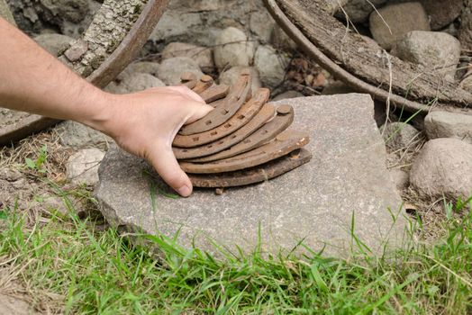 man hand put old rusty iron horseshoe pile on stone outdoor