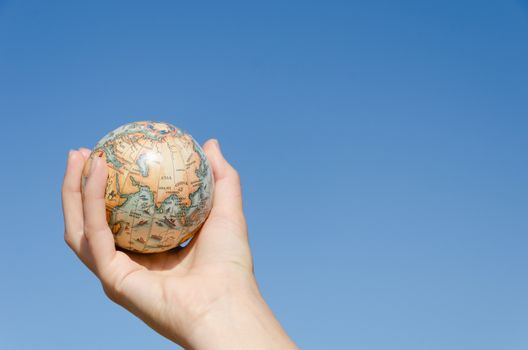 small symbol of global earth in female hand on blue sky background, Asia continent