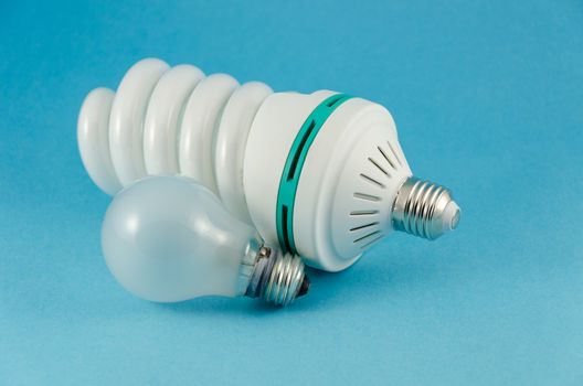 big energy saving spiral lamp and simple incandescent bulb on blue background