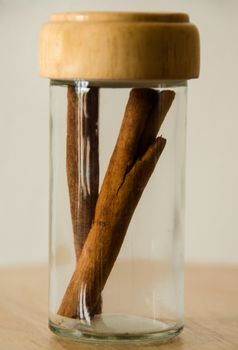 Cinnamon in the glass jar on wooden table, white background. 