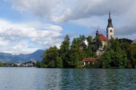 Catholic church situated on an island on Bled lake with mountains and resort on the background 