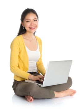 Full body Asian woman in yellow blouse using laptop computer notebook, looking at camera, seated on floor isolated on white background.