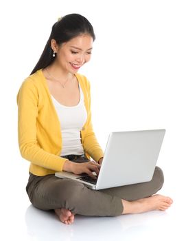 Full body Asian woman in yellow blouse using laptop computer notebook, looking at screen, seated on floor isolated on white background.
