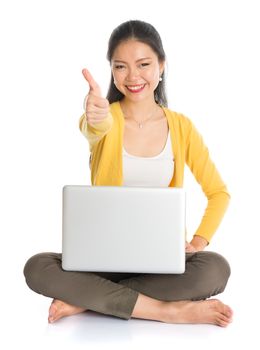 Full body Asian woman in yellow blouse thumb up when using laptop computer notebook, seated on floor isolated on white background.