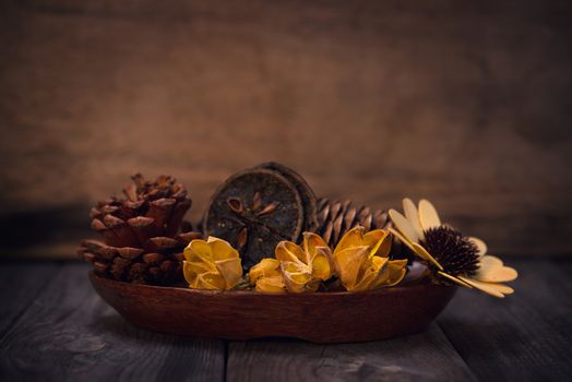 Aromatherapy concept. Dried flowers on wooden bowl in low light ambient setting.