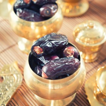 Dried date palm fruits or kurma, ramadan food which eaten in fasting month. Pile of fresh dried date fruits in golden metal bowl.