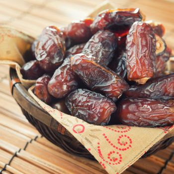 Pile of fresh dried date fruits in bamboo basket. Dried date palm fruits or kurma, ramadan food which eaten in fasting month. 