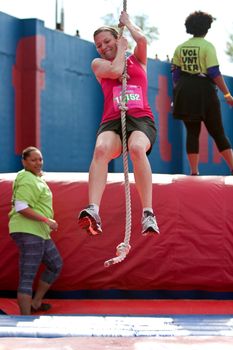 Atlanta, GA USA - April 5, 2014:  A young woman holds on and swings with a rope in one of the events at the Ridiculous Obstacle Challenge (ROC) 5K race.