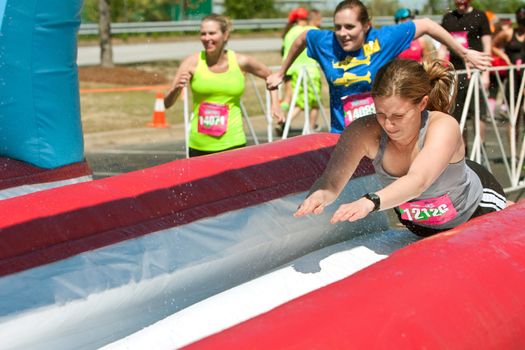 Atlanta, GA USA - April 5, 2014:  Young women dive onto a wet plastic slide as they make their way through the obstacles at the Ridiculous Obstacle Challenge (ROC) 5K race.