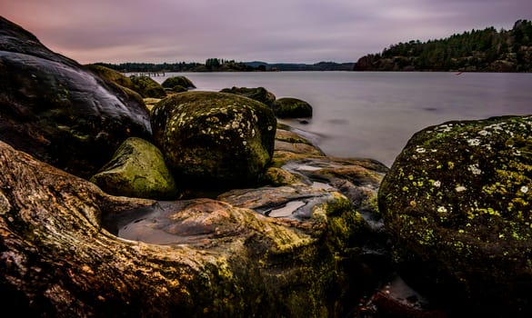 Coastal sunset with soft waves washing over the beach and rocks