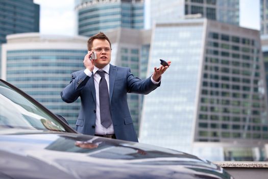businessman on background of office near the car gives instructions over the phone and shows the hand