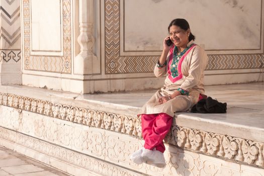 Indian woman in traditional dress is seen chatting happily on the phone st the Taj Mahal in the early morning light
