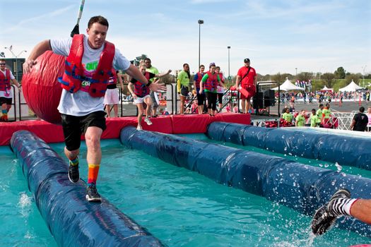 Atlanta, GA USA - April 5, 2014:  A man sprints across a narrow pipe trying to run through the wrecking balls event, at the Ridiculous Obstacle Challenge (ROC) 5K race.