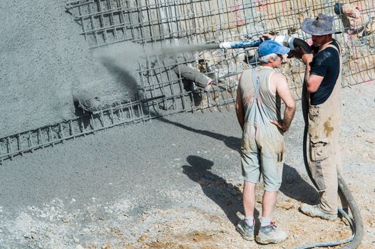 OSTFILDERN-SCHARNHAUSEN, GERMANY - MAY 22, 2014: A worker is aiming a pump tube while pouring concrete against the earth walls of a construction site whilst his colleague is chatting with him on May, 22, 2014 in Ostfildern-Scharnhausen near Stuttgart, Germany.
