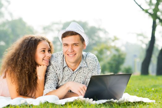 couple lying together in a park, working together on a laptop