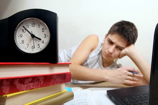 Tired Teenager preparing for Exam in the Night at the Home. Focus on the Clock
