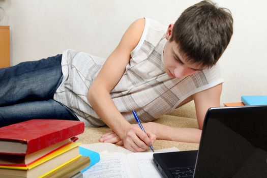 Teenager doing Homework on the Sofa with Laptop and many Books