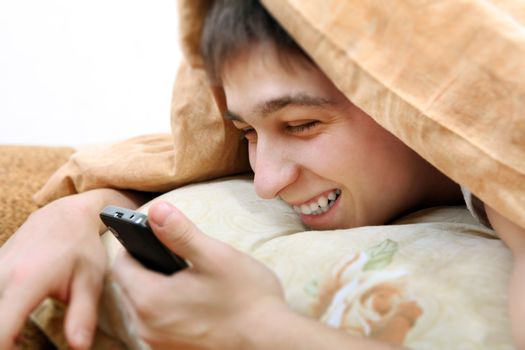 Cheerful Teenager with Cellphone under Blanket at the Home