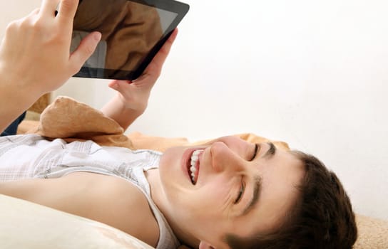 Cheerful Teenager using the Tablet Computer on the Sofa at the Home