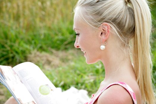 young attractive woman is sitting in the open countryside and reads a magazine