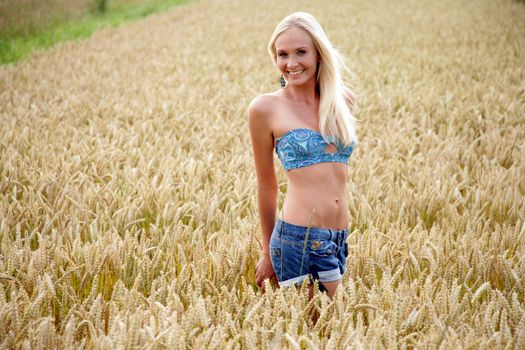 Young woman with bikini top and hot pants standing in a wheat field She looks relaxed and cheerful.