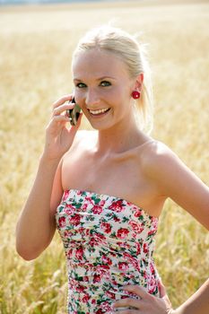 Young attractive woman is standing in a wheat field and speaks into her mobile phone. She looks happy and relaxed.