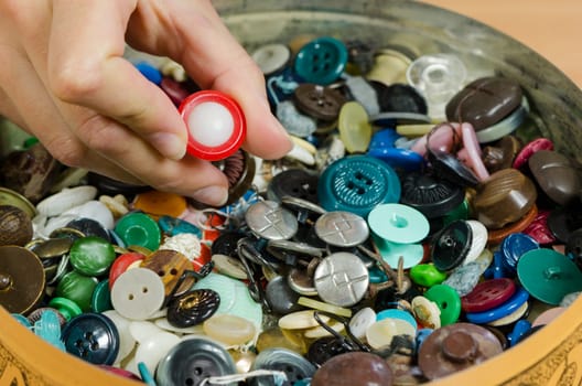 Dish full of various colorful buttons and seamstress needlewoman finger pick it for wear.