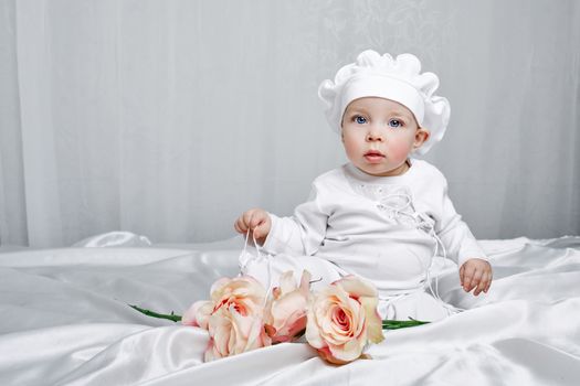 Little girl sitting on silk sheets lie at the feet of flowers