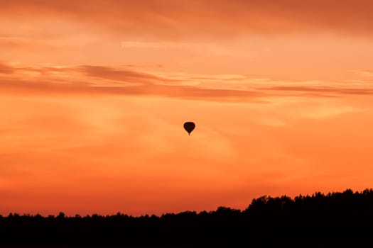 Hot air balloon flying at orange sunset sky